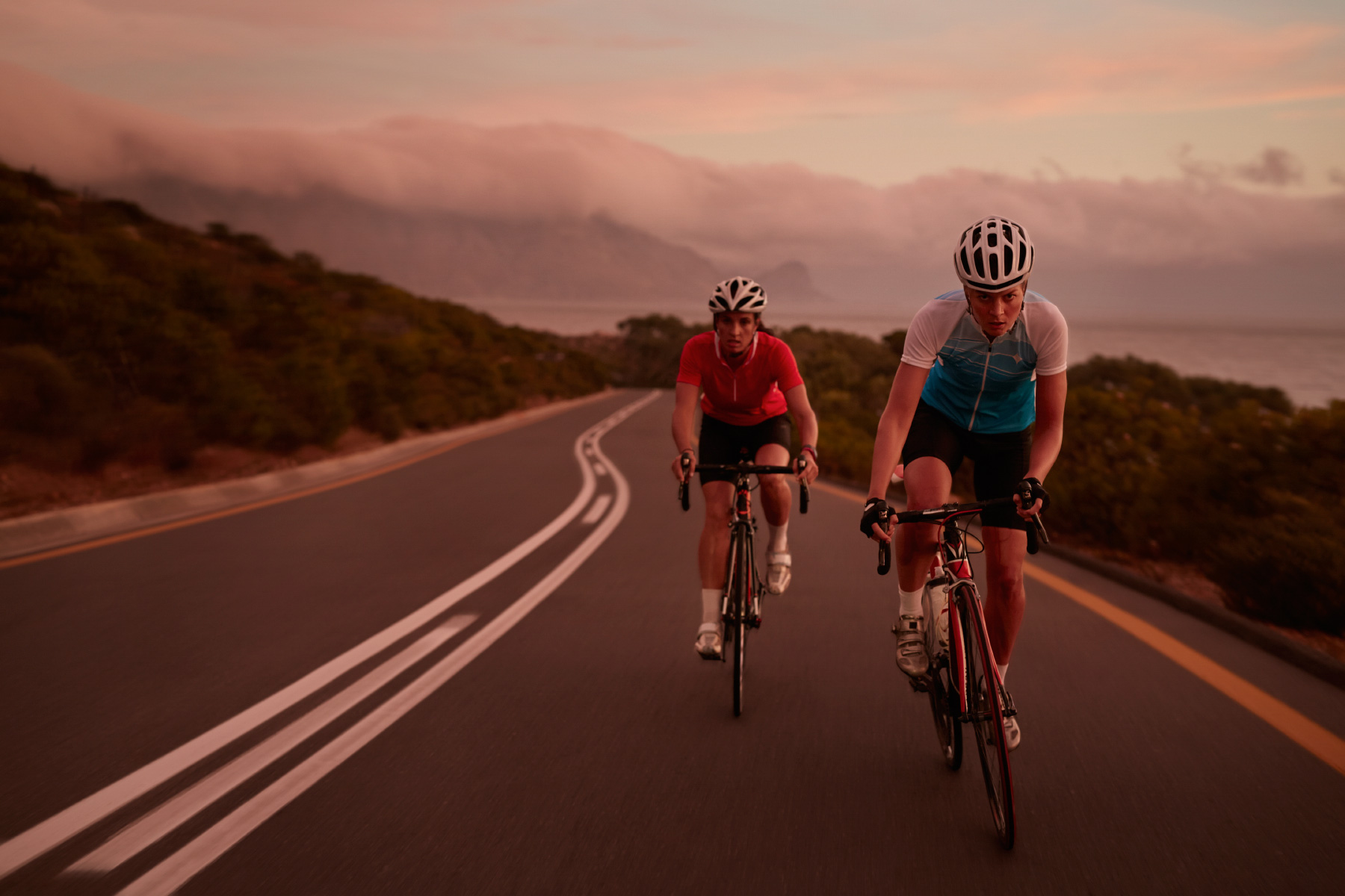 Pro female cyclists sprinting on road bikes at  last light