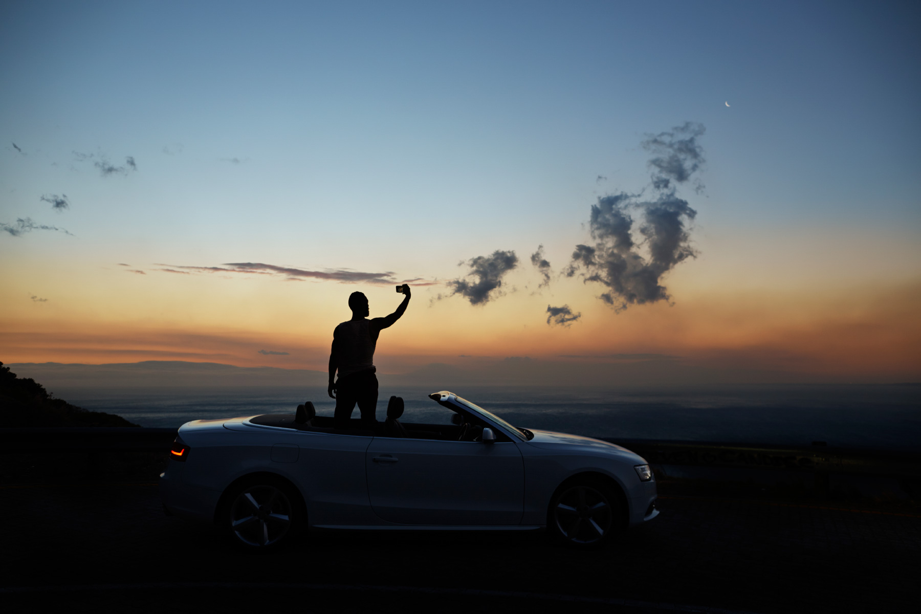 Man taking picture of sunset in his convertible car