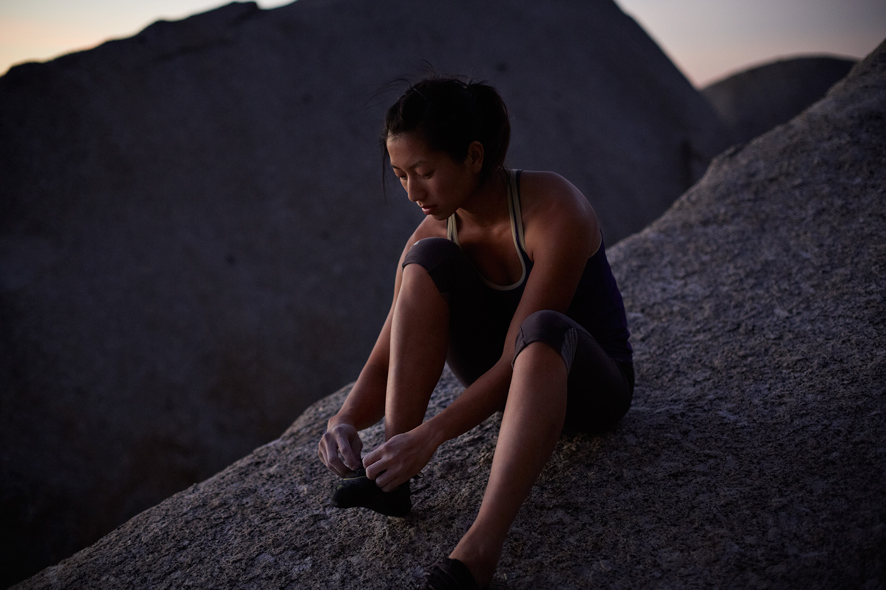 Female climber sitting on big boulder, tying shoes a